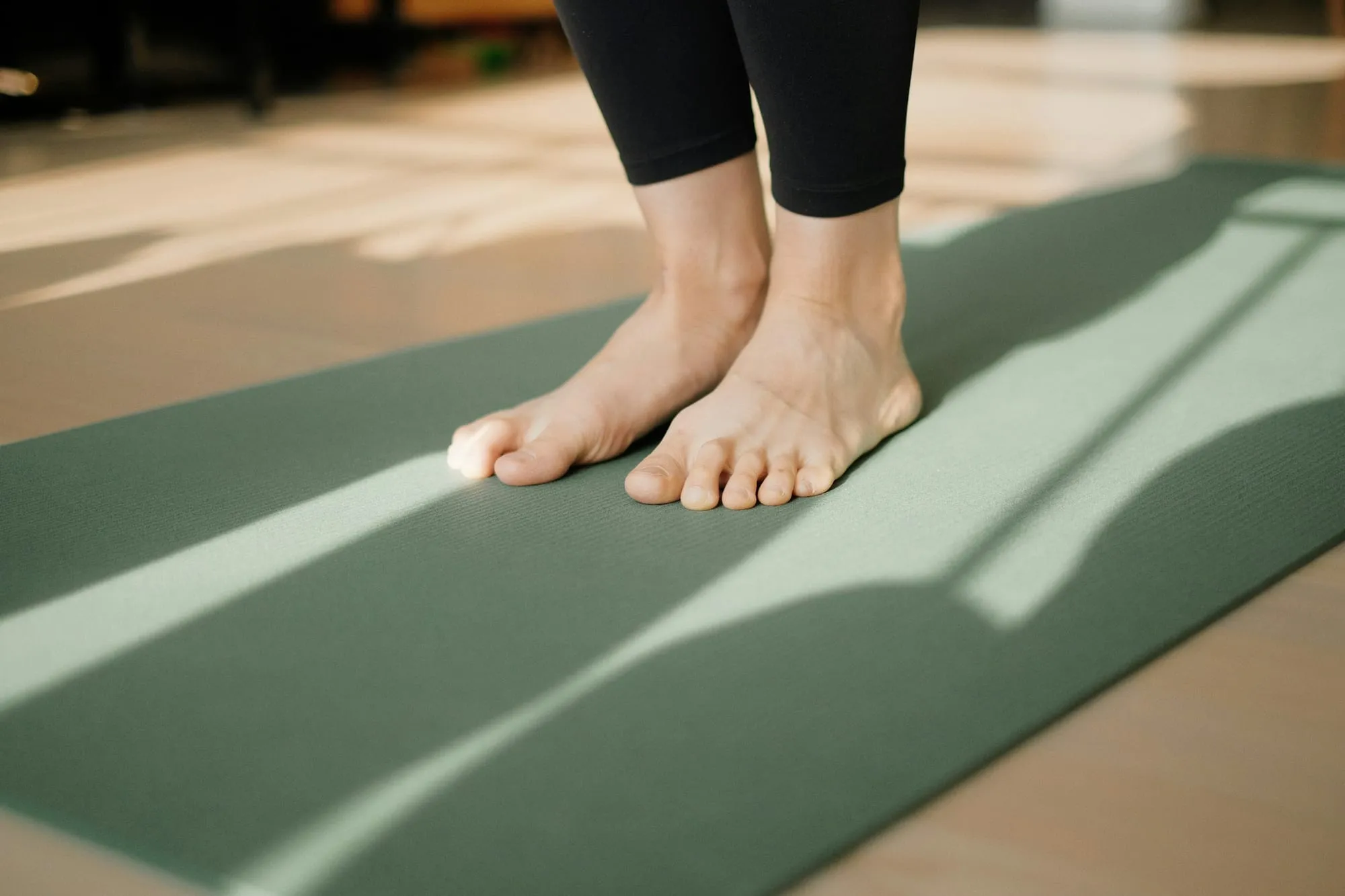 Nackte Füße auf einer grünen Yogamatte im Sonnenlicht